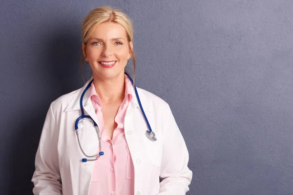 在灰色背景下与复印空间站在一起的微笑女医生穿上医疗礼服的镜头 — 图库照片