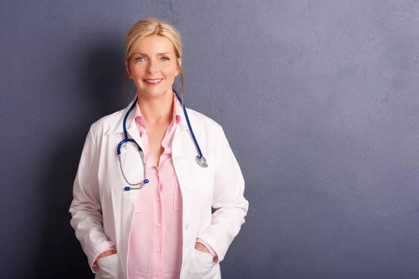 在灰色背景下与复印空间站在一起的微笑女医生穿上医疗礼服的镜头 — 图库照片