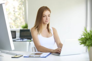 Düşünceli arıyorum ve ofis masa başında otururken dizüstü bilgisayarda yazarak genç profesyonel kadın.