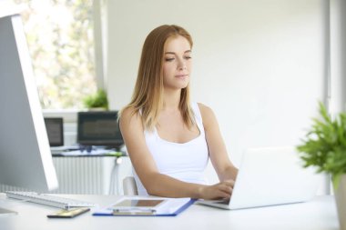 Laptop 'un klavyesinde yazan ve yeni bir proje üzerinde çalışan çekici genç iş kadını..