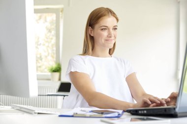 Ofis masasında otururken ve internette çalışırken gülümseyen genç iş kadınının fotoğrafı.. 