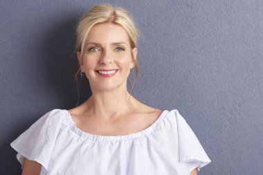 gri duvara beyaz bluz giyen güzel olgun gülümseyen kadın
