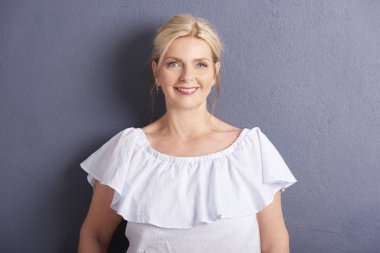 gri duvara beyaz bluz giyen güzel olgun gülümseyen kadın