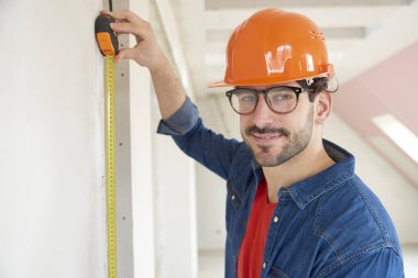 İnşaat alanında çalışırken mezura kullanan genç adamın portresi. 