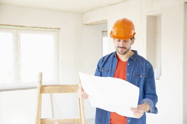 Genç erkek mühendis holding blueprint inşaatı yerinde dururken elinde portresi. 