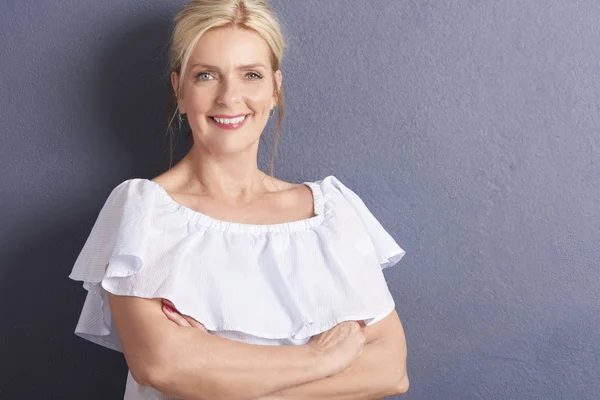 gri duvara beyaz bluz giyen güzel olgun gülümseyen kadın