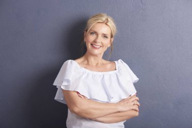 Kameraya bakarak ve karşı poz gri duvara gülümseyen katlanmış silah ile güzel bir yaşlı kadın portresi. 