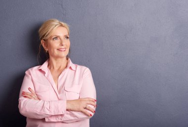 Güzel yaşlı kadın katlanmış silah kopya alanı ile gri duvara karşı poz ile portresi