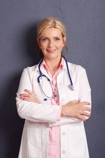 灰色の背景で腕を組んで立っている先輩女性医師の肖像画 — ストック写真