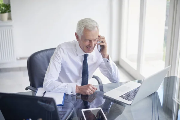 Executivo Empresário Sênior Falando Smartphone Enquanto Trabalhava Laptop Escritório — Fotografia de Stock