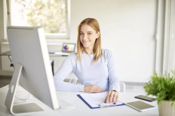微笑的年轻女商人坐在电脑前 摆在明亮的办公室 — 图库照片