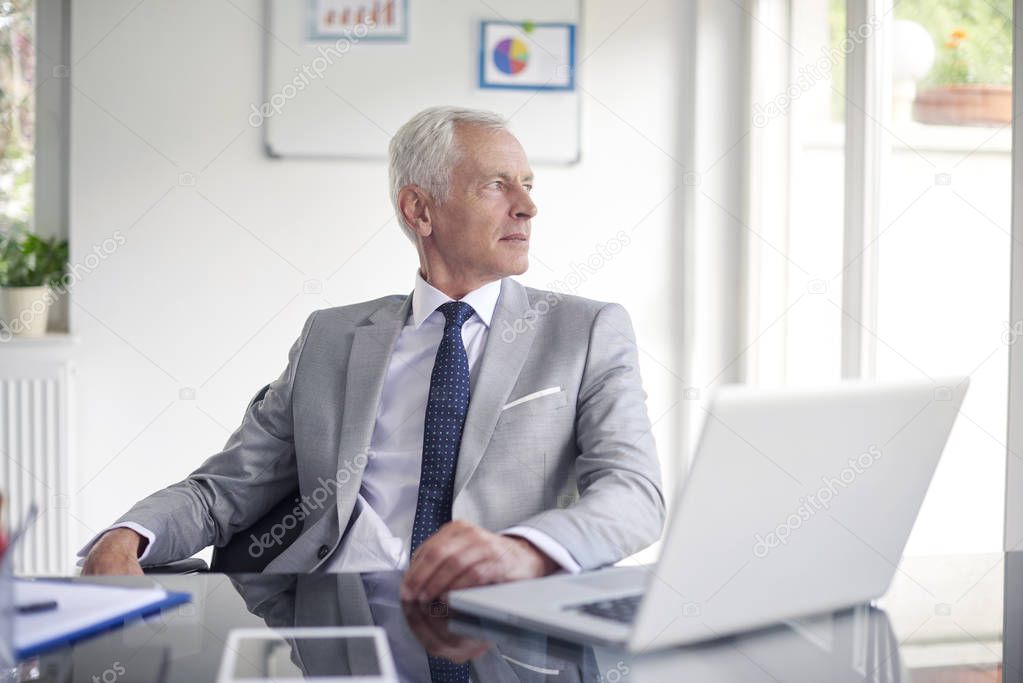 Executive senior businessman posing at office desk behind laptops