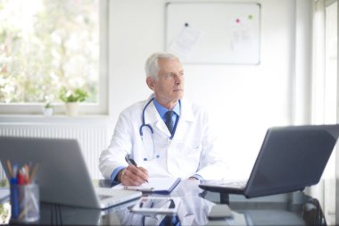 Düşünceli Danışmanlık Oda oturma ve tıbbi tanı aşağı yazma sırasında arıyorum erkek doktor portresi.