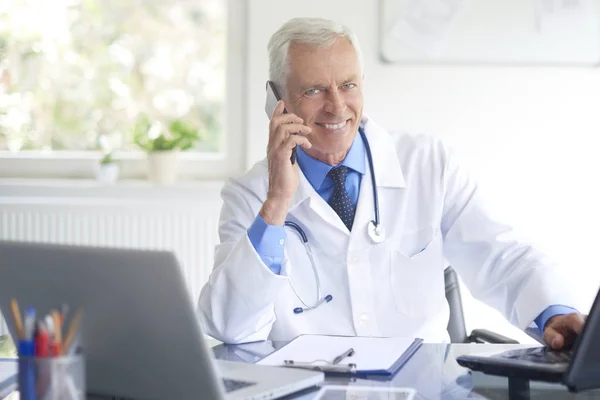 Sorridente Médico Masculino Sentado Mesa Consultório Falando Telefone Olhando Para — Fotografia de Stock