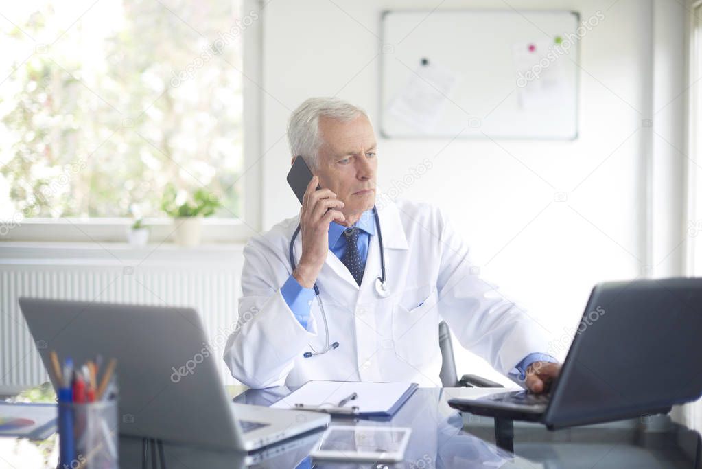 male doctor sitting at consulting room and talking on phone. 