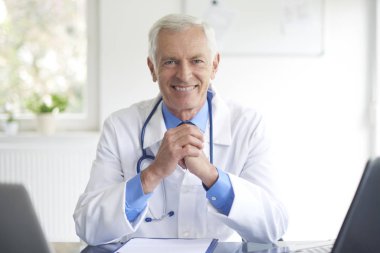 Yaşlı erkek Doktor tıbbi sabahlık sağlık odası oturma giyiyor