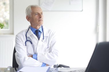 Yaşlı erkek Doktor tıbbi sabahlık sağlık odası oturma giyiyor