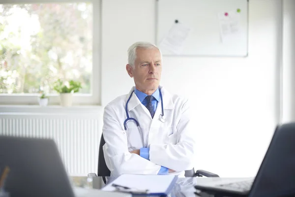 Ηλικιωμένος Γιατρός Αρσενικό Φοράει Ιατρικές Ρόμπα Που Κάθεται Στο Ιατρείο — Φωτογραφία Αρχείου