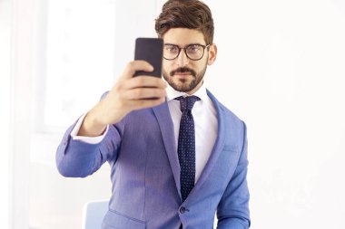 Cep telefonunu kullanarak ve ofiste çalışırken kendi kendine portre çekici genç işadamı portre çekim. 