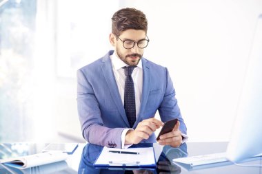 Onun cep telefonu ve kısa ofis masası mesaj kullanarak yakışıklı genç işadamı.