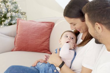 Mutlu genç aile ile onların bebek kız kanepede oturan ve Noel zamanda birbirlerinin şirket zevk. 