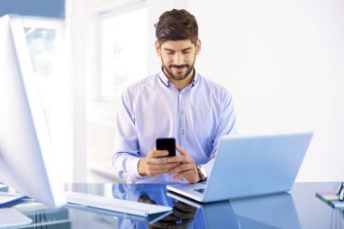 Ofis masasında dizüstü bilgisayarının arkasında otururken tişört giyen genç bir işadamı..