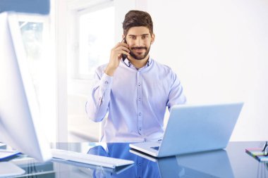 Ofis Masası diz üstü arkasında oturan ve bir telefon görüşmesi sırasında gömlek giymiş mutlu işadamı. 