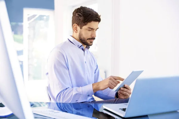 年轻商人穿着华而不实的衬衫坐在办公室笔记本电脑后面 使用数码平板电脑的肖像 办公室里的多任务工作 — 图库照片