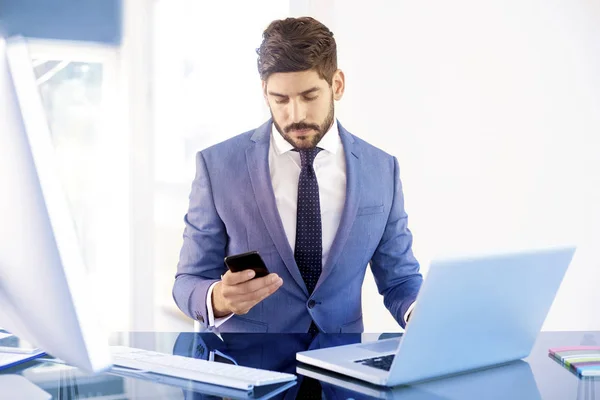 Executive financial advisor businessman wearing suit and using his cell phone while sitting at office desk and working on an investment project.