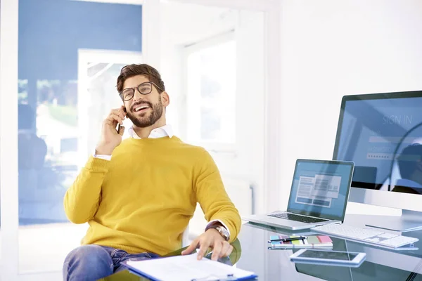 Portrait of executive young professional man making phone call while sitting in office. Young businessman talking on mobile phone.