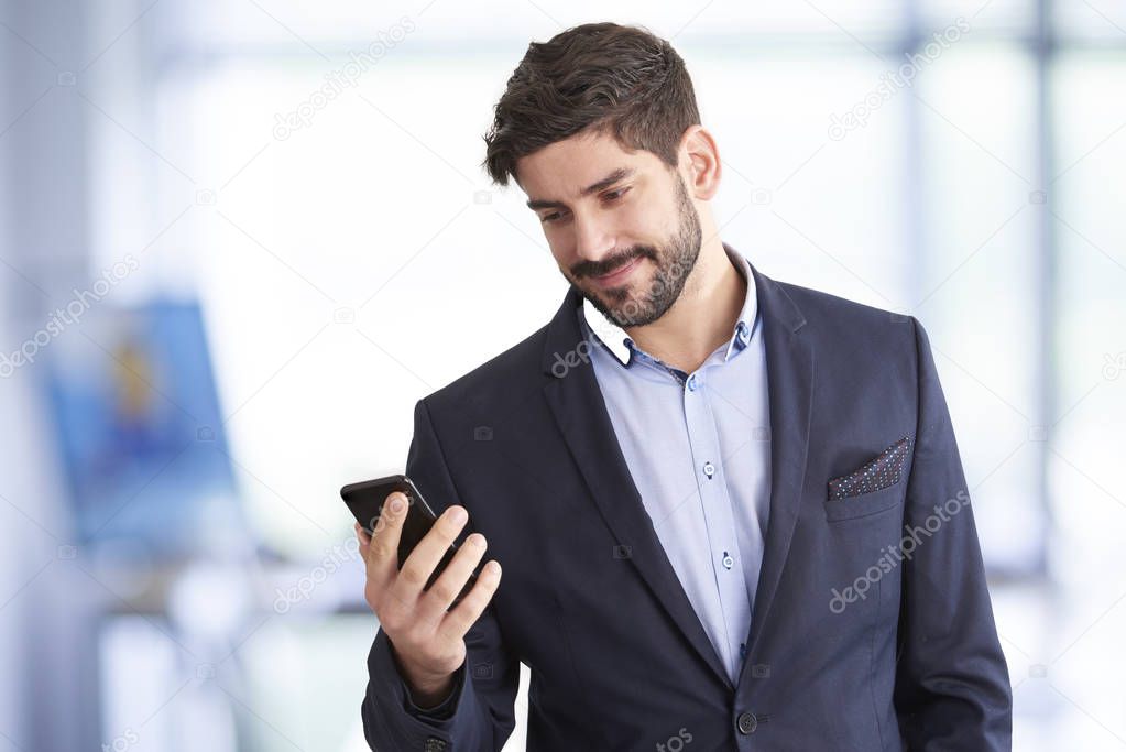 handsome young businessman wearing suit jacket and standing at isolated white background and browsing mobile phone