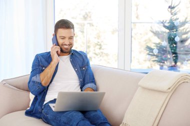 Evdeki kanepede otururken bilgisayarını kullanan yakışıklı bir gencin portresi.. 