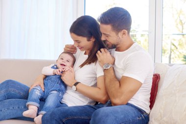 Mutlu genç aile oturan Divan bebek kızları ile vurdu ve evde rahatlatıcı keyfini çıkarın. 