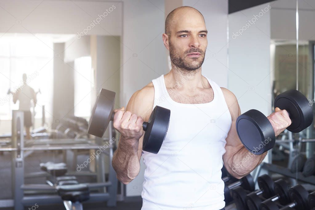 Close-up of man in the gym using barbells and doing dumbbell exercises to create more muscular body.