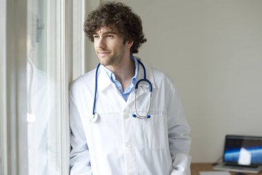 Genç bir erkek doktor doktor odada ve pencereden bakarak kadeh. 