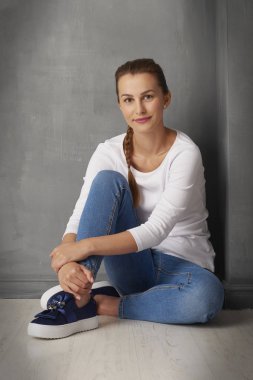 Tam uzunlukta stüdyo portre sevimli genç bir kadın kopya alanı ile gri duvara oturan. 