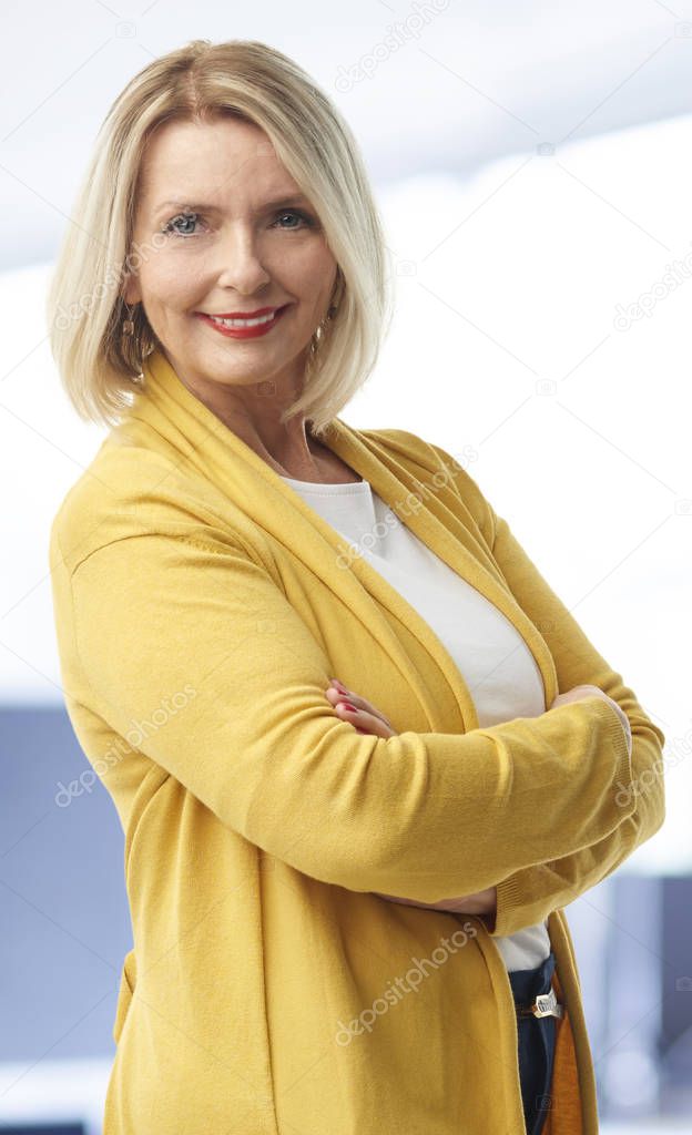 A beautiful middle aged financial assistant businesswoman wearing casual clothes and smiling to you while standing with arms crossed at the office. 