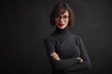 Rulo yakın çekim portre çekim giyen güzel genç kadın boyun kazak ve gözlük dururken koyu arka plan. 