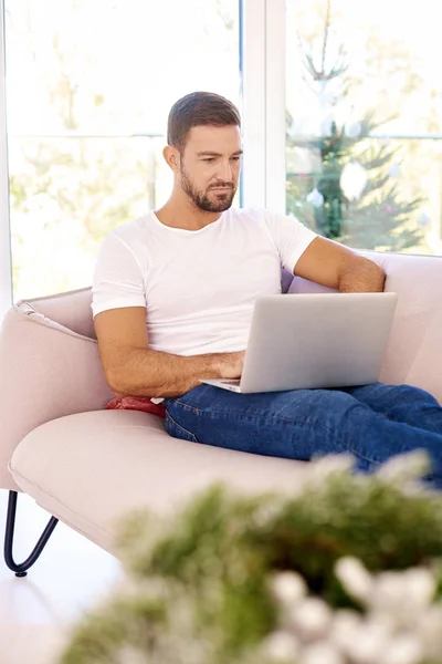 Portraitaufnahme eines hübschen jungen Mannes, der im Sitzen auf seinem Laptop surft — Stockfoto