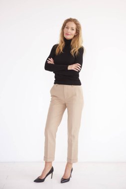 Izole beyaz arka planda dururken rulo boyun kazak giyen sarı saçlı güzel olgun kadın tam uzunlukta portre çekimi.