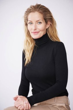 Çekici orta yaşlı kadının kameraya bakıp izole beyaz arka planda otururken gülümseyen portresi.