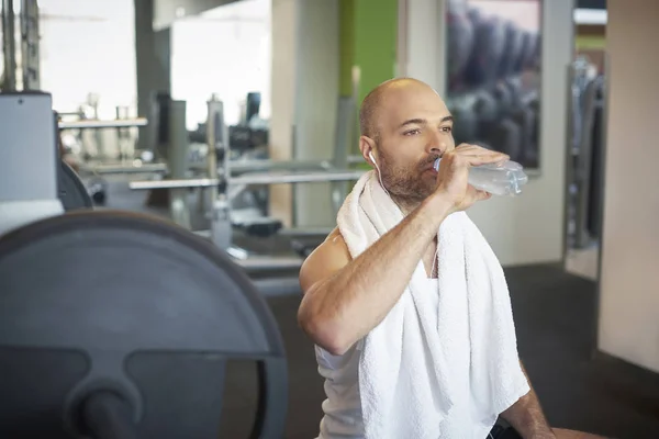 Спортивный человек расслабляется в тренажерном зале и пьет бутылку воды — стоковое фото