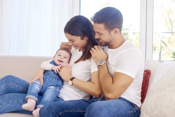 Cheerful young family with their cute baby girl sitting on sofa — Stock Photo, Image