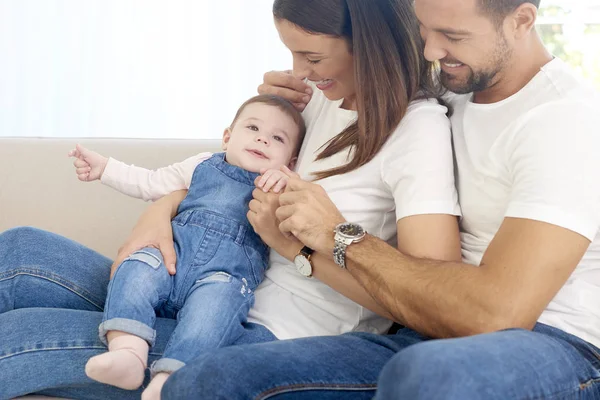 Fröhliche junge Familie mit ihrem süßen Baby-Mädchen auf dem Sofa — Stockfoto