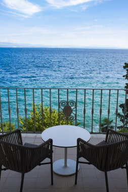 Sandalyeler ve masalarla deniz manzaralı harika bir balkon.