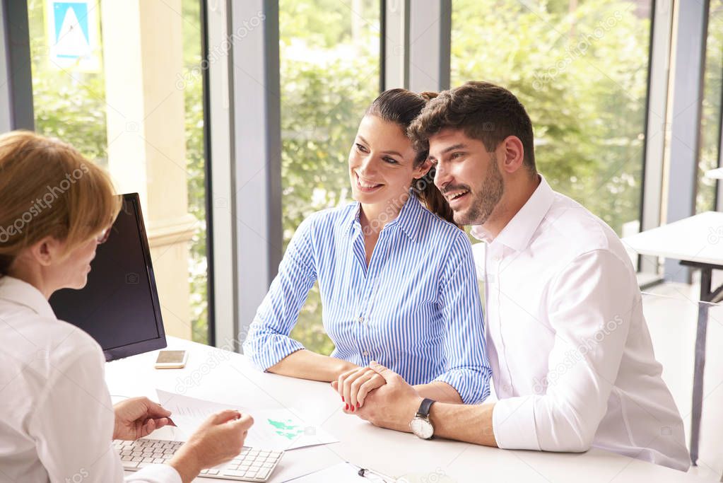 Financial advisor businesswoman sitting at office desk in front of computer and consulting with young couple about finance tips.