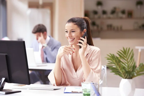 Felice donna d'affari dando una chiamata e lavorando sul computer nel — Foto Stock