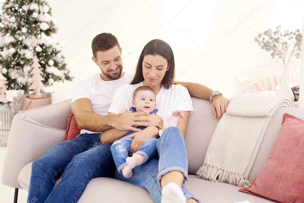 Lovely family with their baby girl relaxing on sofa at home duri