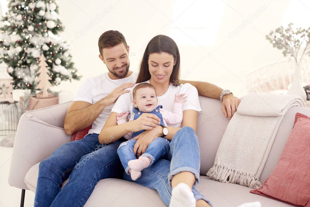 Lovely family with their baby girl relaxing on sofa at home duri