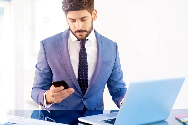 Executive financial advisor businessman wearing suit and using his cell phone while sitting at office desk and working on an investment project.